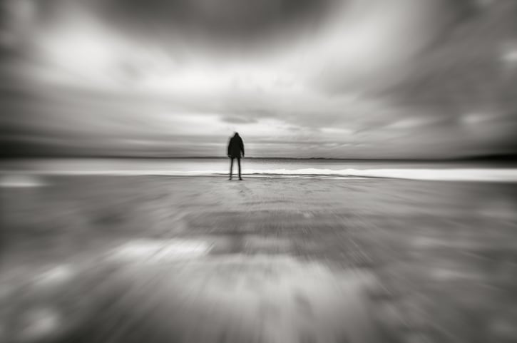 Silhouette of person standing head down on deserted beach in wintertime, motion blur.